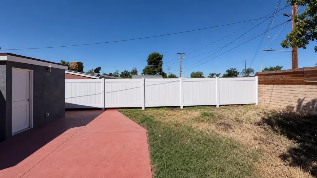 A satellite dish and rooftop equipment sit above this White vinyl fence tracing the yard's rear boundary in Canyon Country