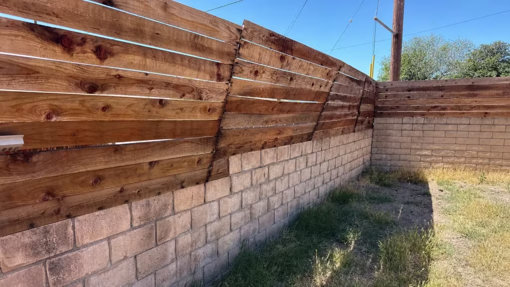 Before installation, uneven horizontal wood boards are attached above a tan block wall around a dry yard.