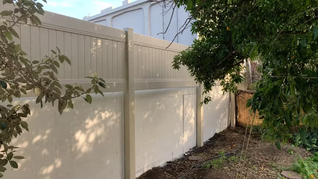 Tan vinyl privacy fence panels mounted atop an existing block wall beside a reed screen in Whittier