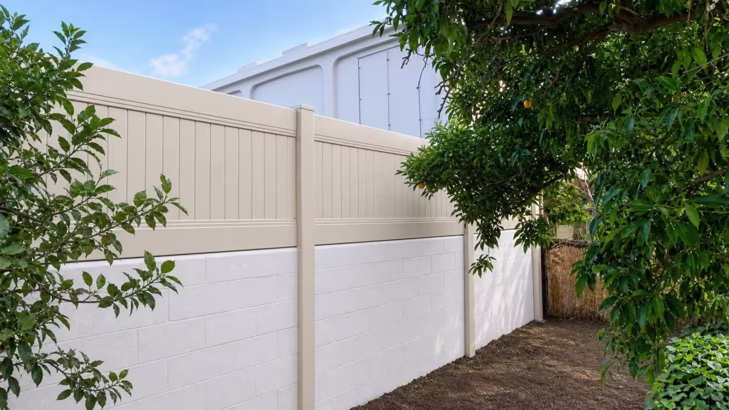 A white building rises just beyond this Tan vinyl privacy fence mounted on the Whittier block wall