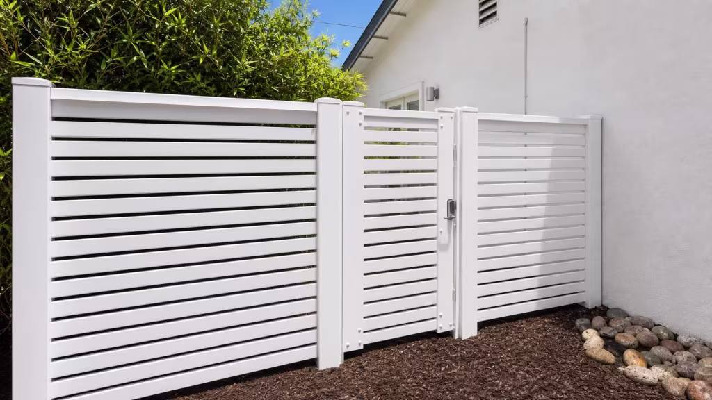 Bamboo-like planting grows beside this White vinyl horizontal picket fence along a narrow side yard
