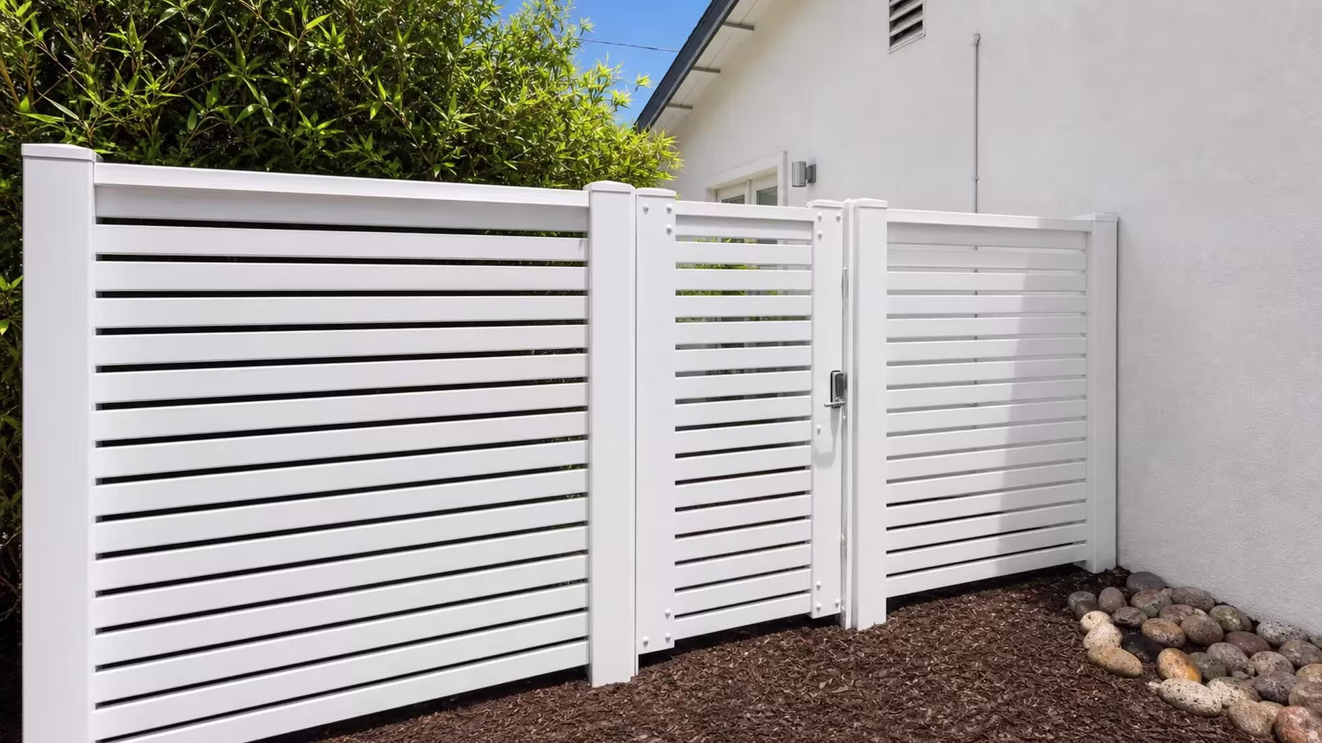 Bamboo-like planting grows beside this White vinyl horizontal picket fence along a narrow side yard