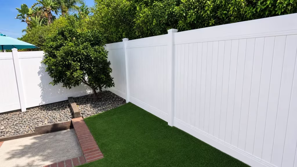 A turquoise patio umbrella stands near this White vinyl privacy fence turning past a mature citrus tree in Laguna Hills