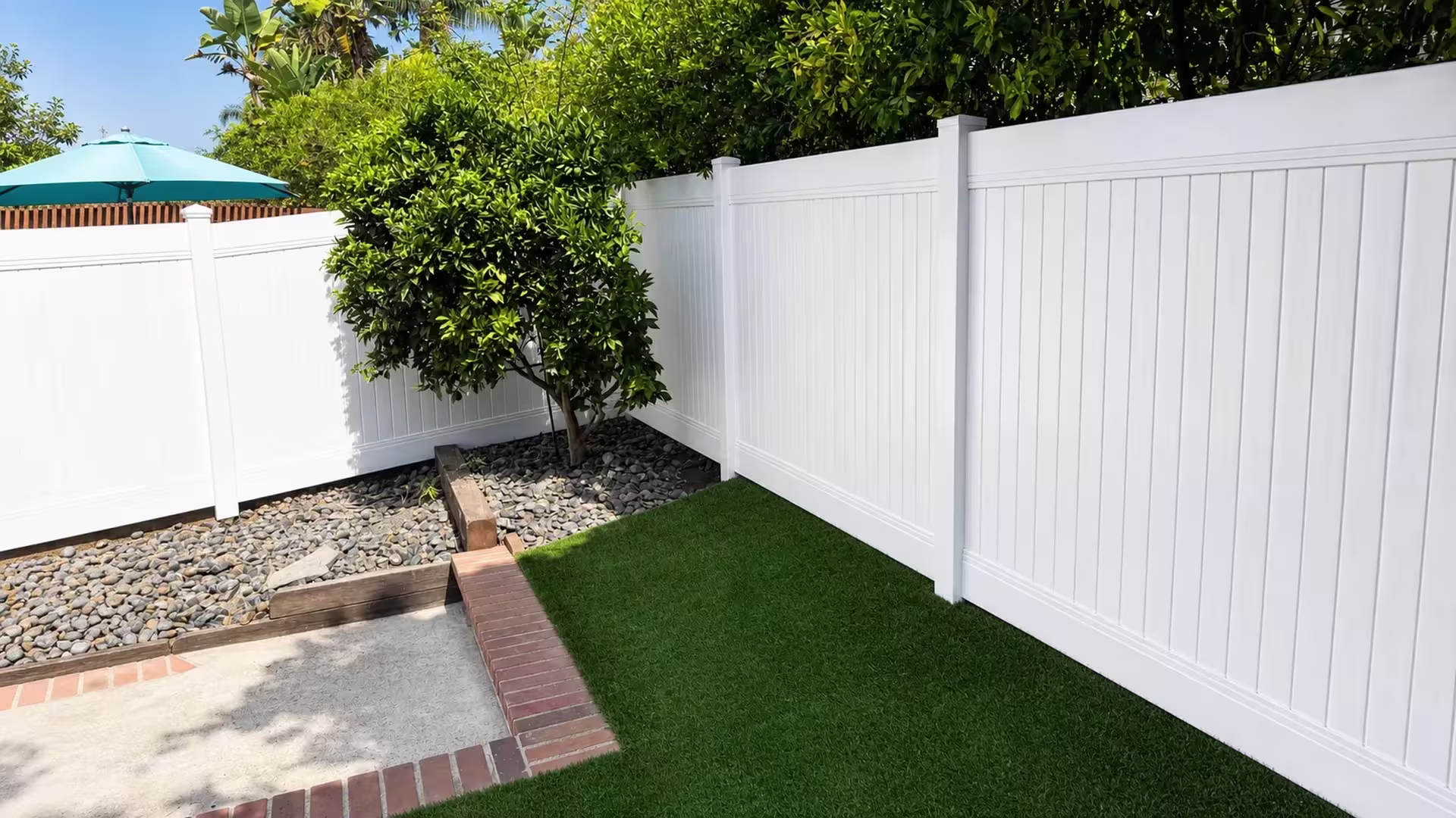 A stone-filled planting bed borders this White vinyl privacy fence wrapping around the corner in Laguna Hills