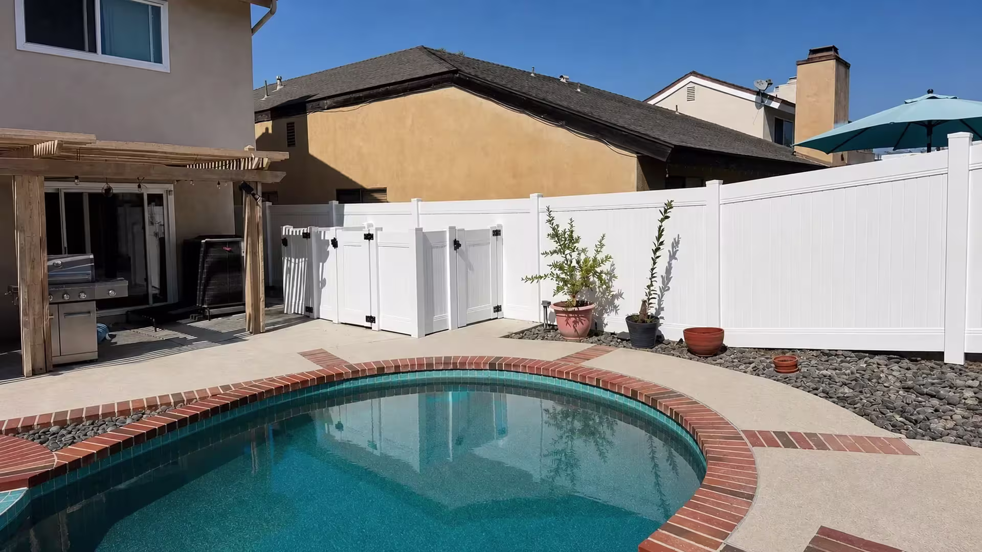 This Laguna Hills patio has river-rock beds and a sliding door beside its White vinyl privacy fence