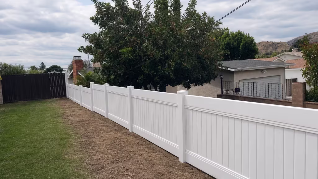 A black metal gate and garage stand beside this White vinyl privacy fence running diagonally in Sunland