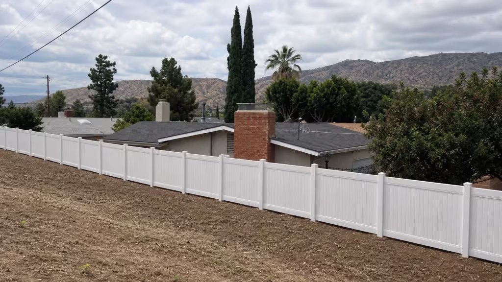 A black metal railing continues past this White vinyl fence as it follows a sloped dirt strip in Sunland