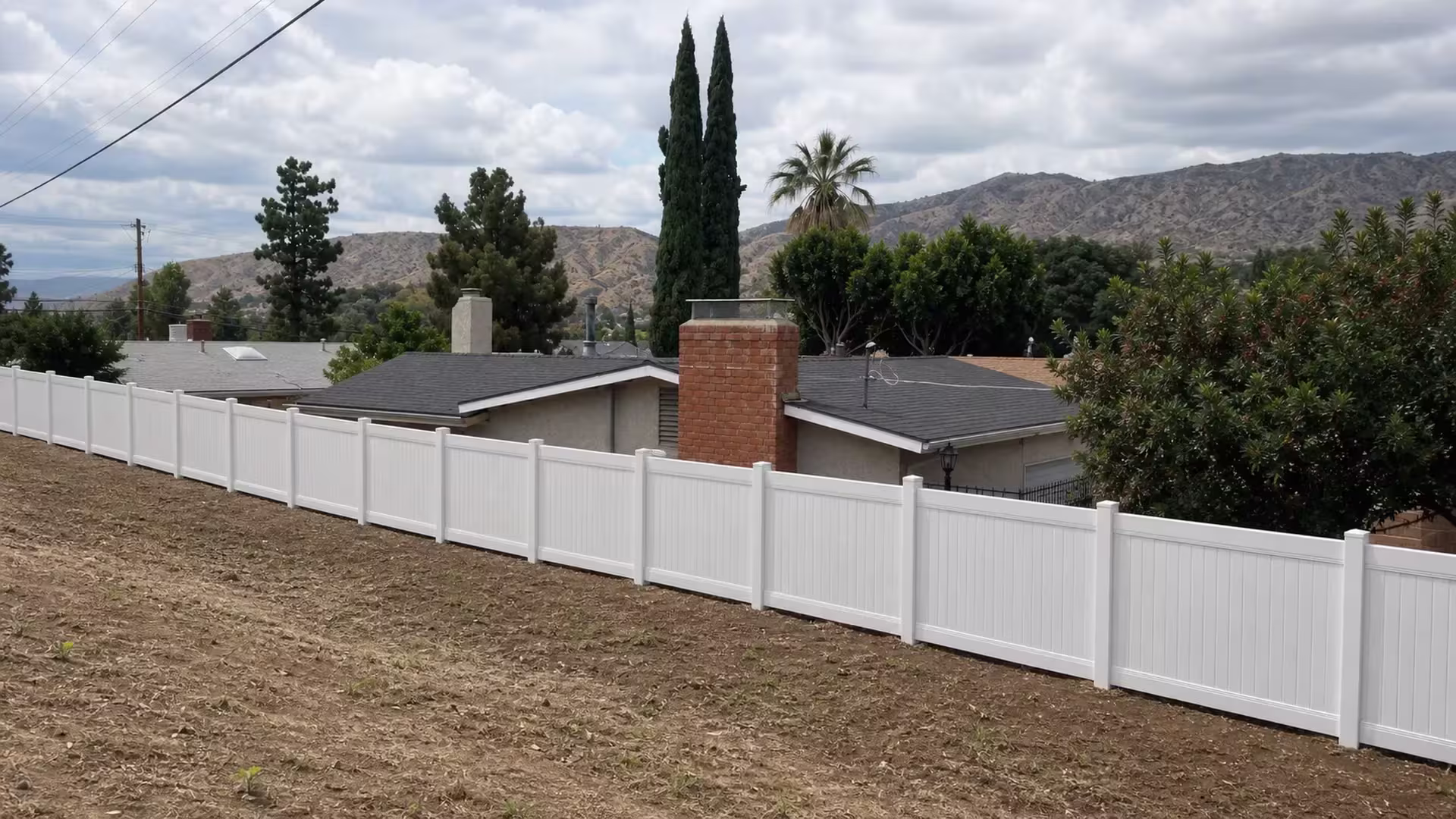 A black metal railing continues past this White vinyl fence as it follows a sloped dirt strip in Sunland