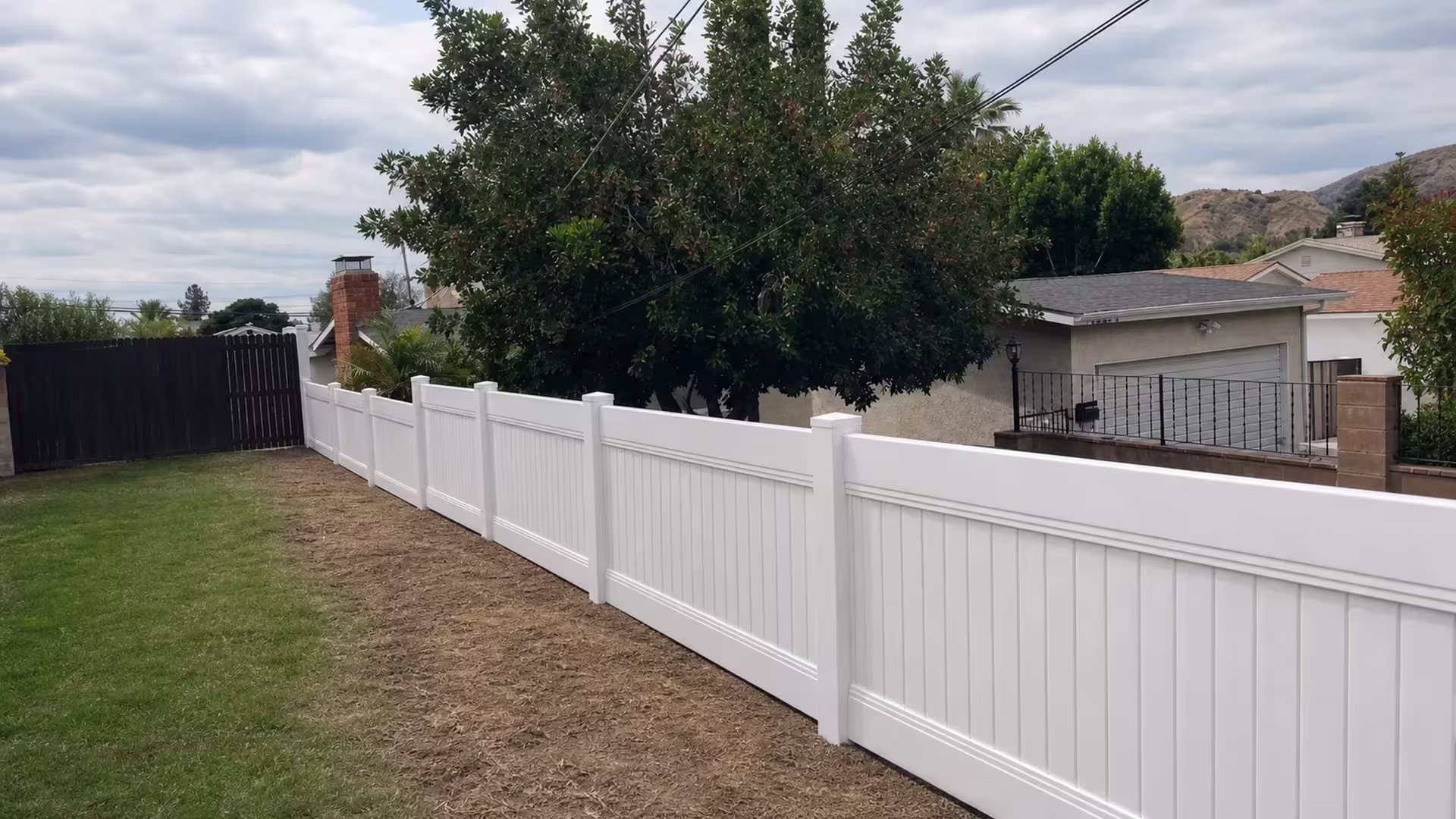 A black metal gate and garage stand beside this White vinyl privacy fence running diagonally in Sunland