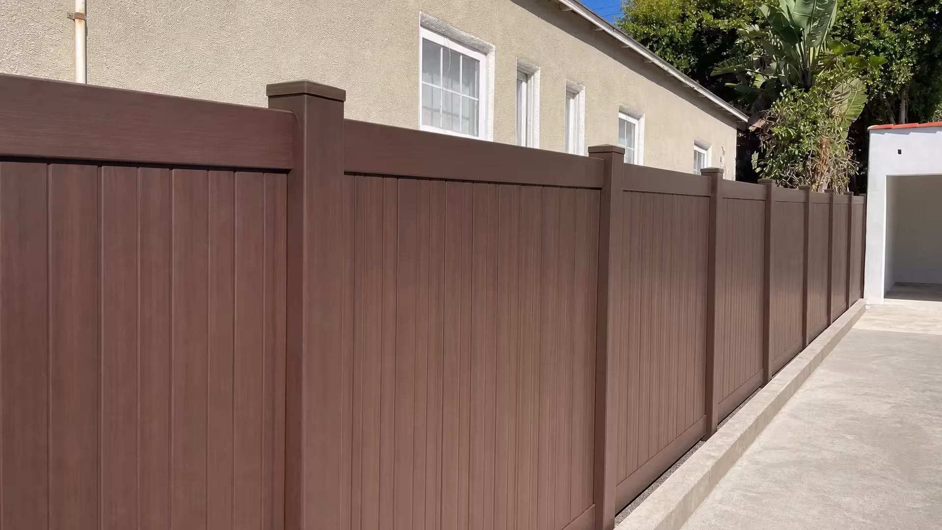 Dark Sequoia vinyl privacy fence boards fit tightly against square posts beside a cream stucco wall in Los Angeles