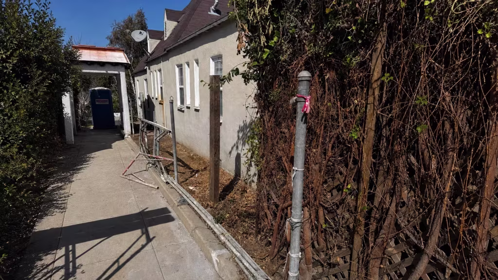 Before installation, a vine-covered wood fence lines a narrow side walkway with temporary construction rails.