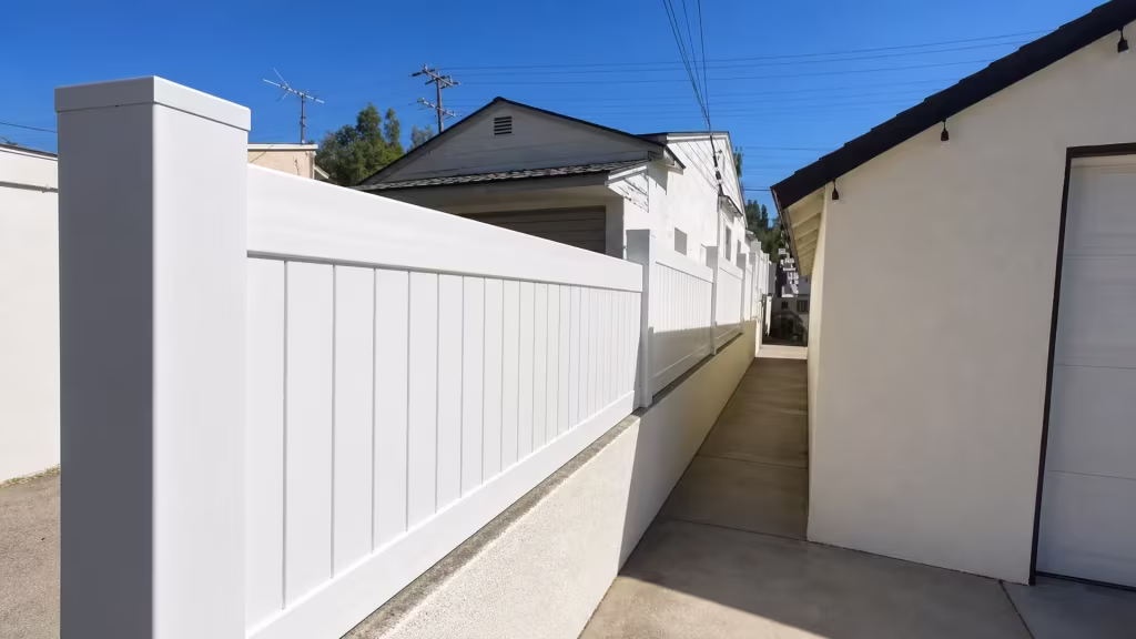 A cream-colored building lines this Glendale property's narrow driveway beside a White vinyl privacy wall topper