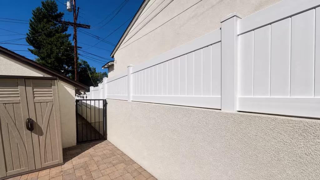 A tan storage shed and a tall evergreen stand beside this Glendale property's White vinyl privacy wall topper