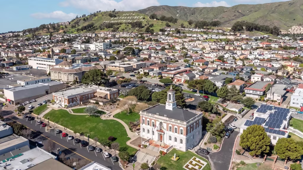 A prominent civic building rises among hillside neighborhoods in this aerial panorama of South San Francisco