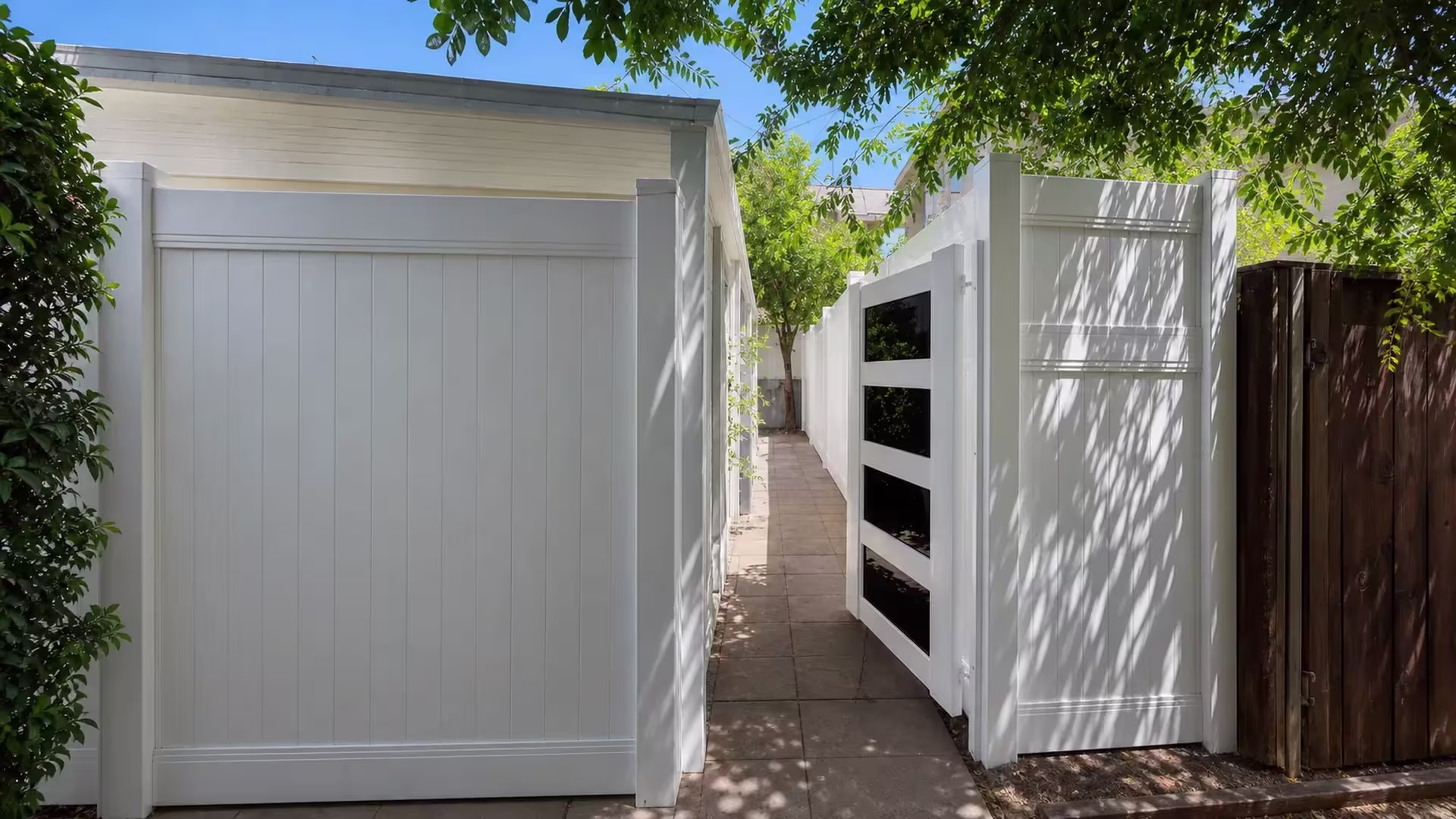 White vinyl privacy-and-acrylic fence has its gate leaf swung open into a West Hollywood passage