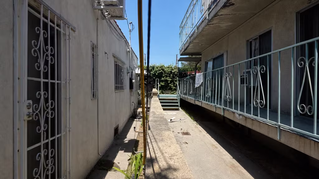 Before installation, a narrow courtyard between apartment buildings is divided by a low block wall and lined with metal railings.
