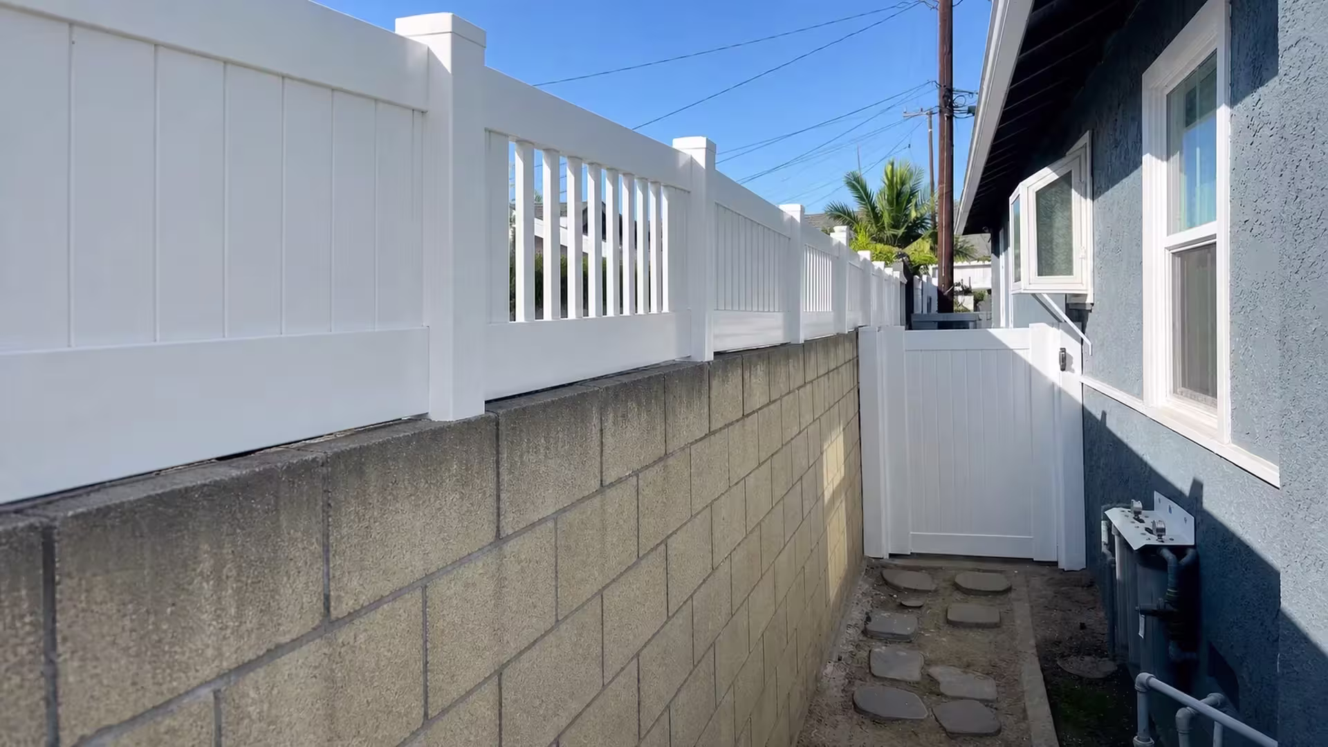 White vinyl privacy gate and wall-top fence close a Long Beach passage where small palms rise beyond it
