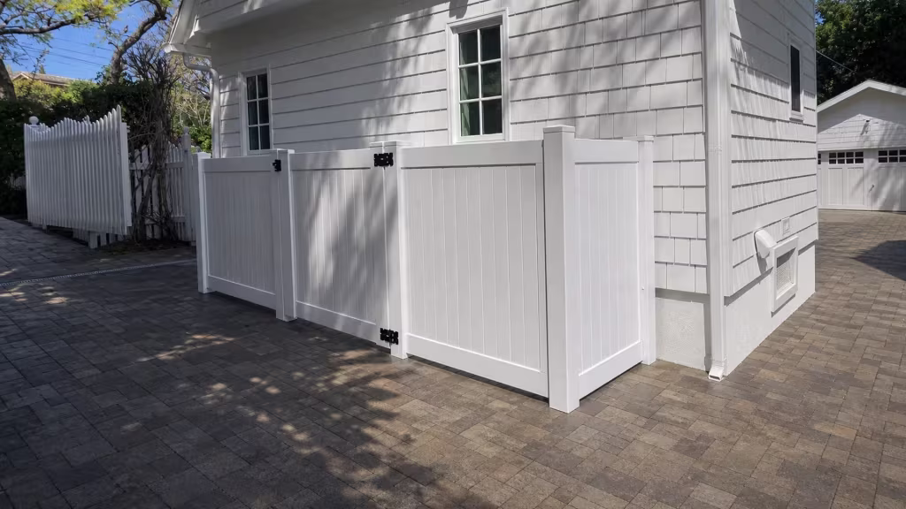 This Los Angeles courtyard is enclosed by a White vinyl fence that passes an existing picket fence near the paver driveway