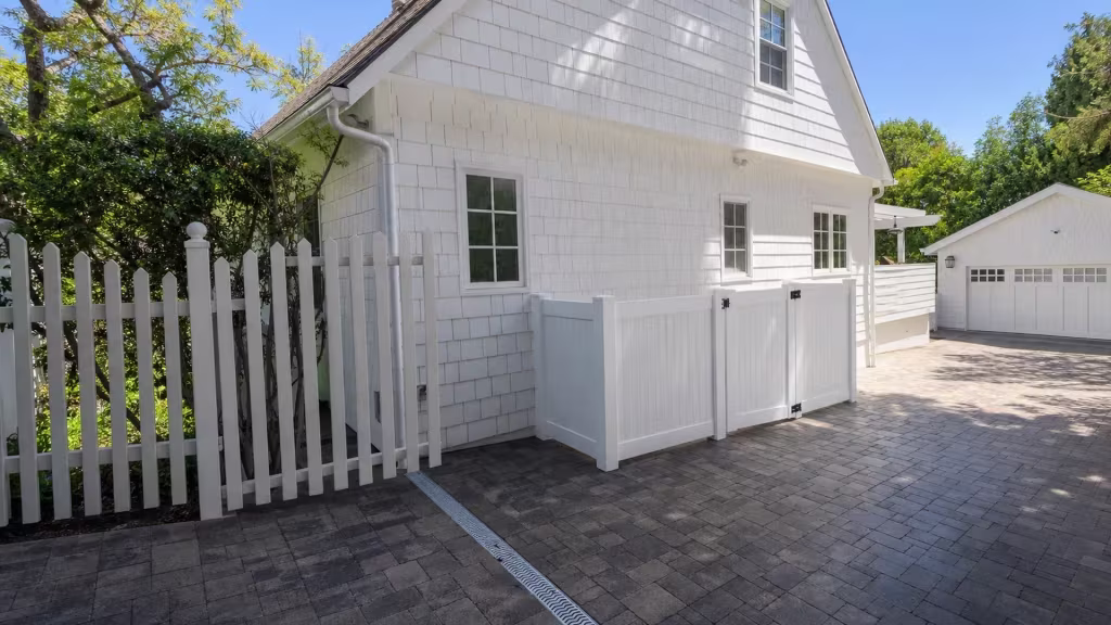 A shingle-sided garage stands beyond this Los Angeles gate, where the White vinyl fence returns to meet the house wall