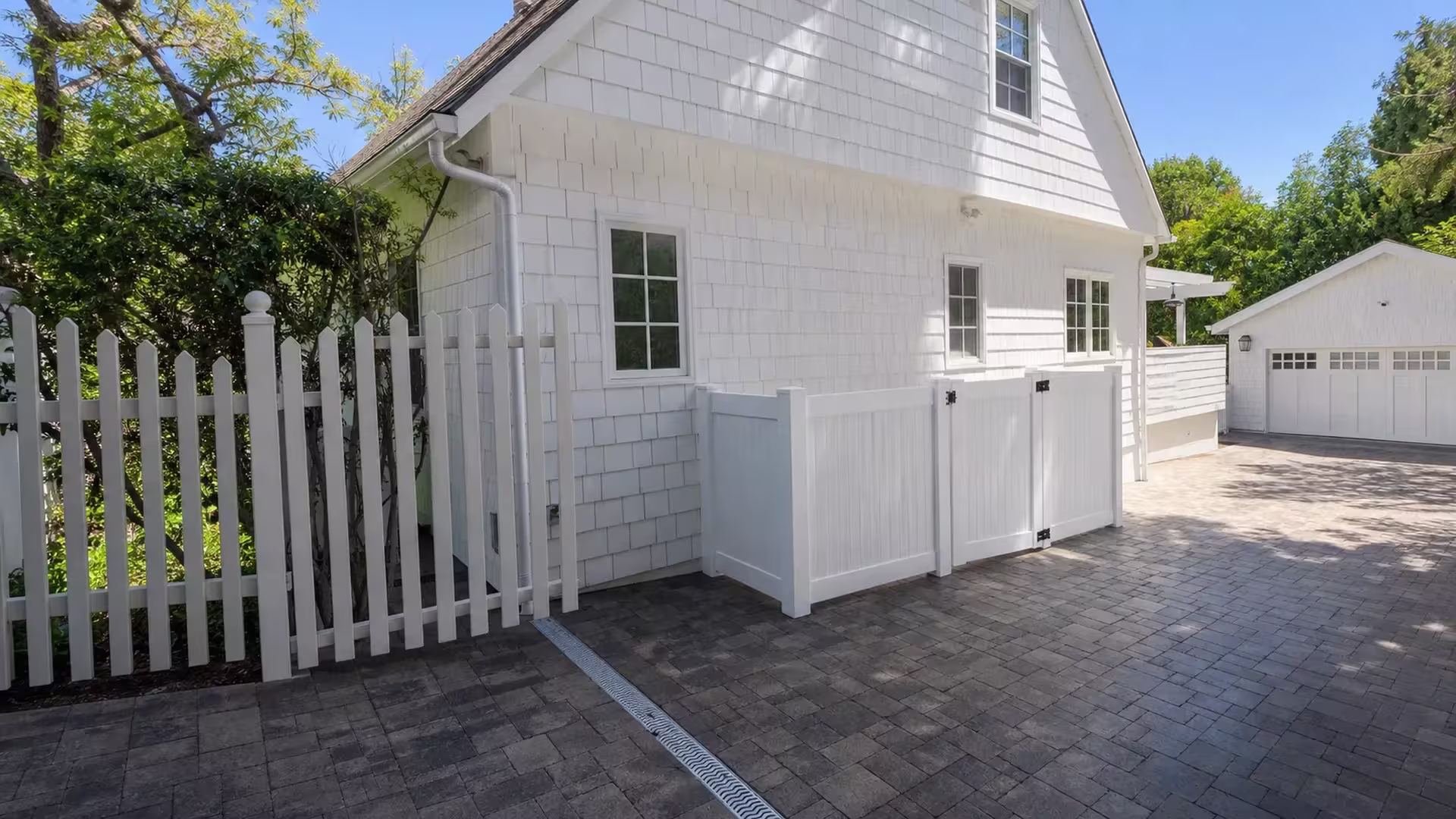 A shingle-sided garage stands beyond this Los Angeles gate, where the White vinyl fence returns to meet the house wall