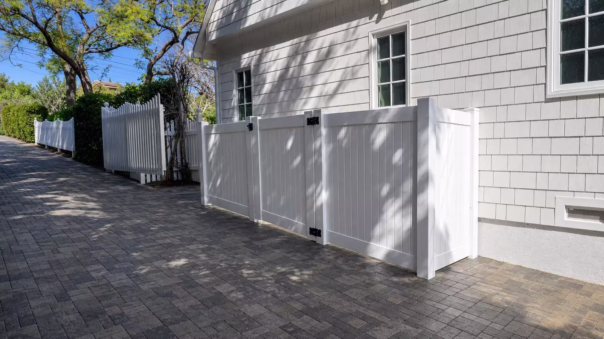 A foundation vent shows on the gray shingle-sided house behind this White vinyl privacy fence and gate in Los Angeles