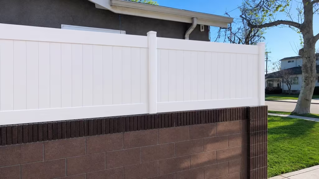 A doorway and downspout trace the stucco house beside a White vinyl privacy wall topper along this Lakewood wall