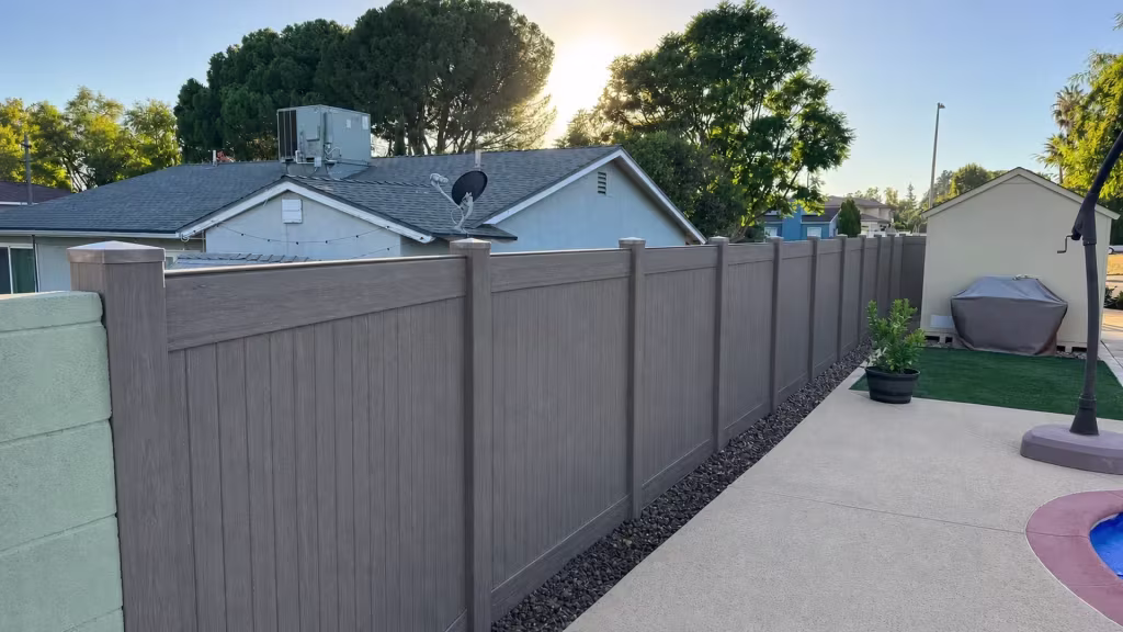 Dark Walnut vinyl privacy fence spanning the yard past a black planter and covered barbecue in Granada Hills