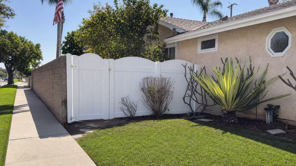 Arched White vinyl privacy fence spans from a tan masonry column to a stucco house in Huntington Beach