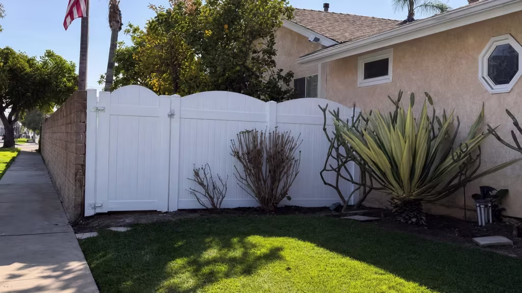 White vinyl privacy fence gate stands beside a tan masonry boundary wall near a sculptural agave planting in Huntington Beach