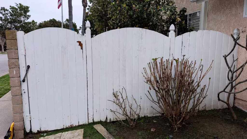 Before installation, a worn white wood fence with curved sections and a gate borders a small front garden.