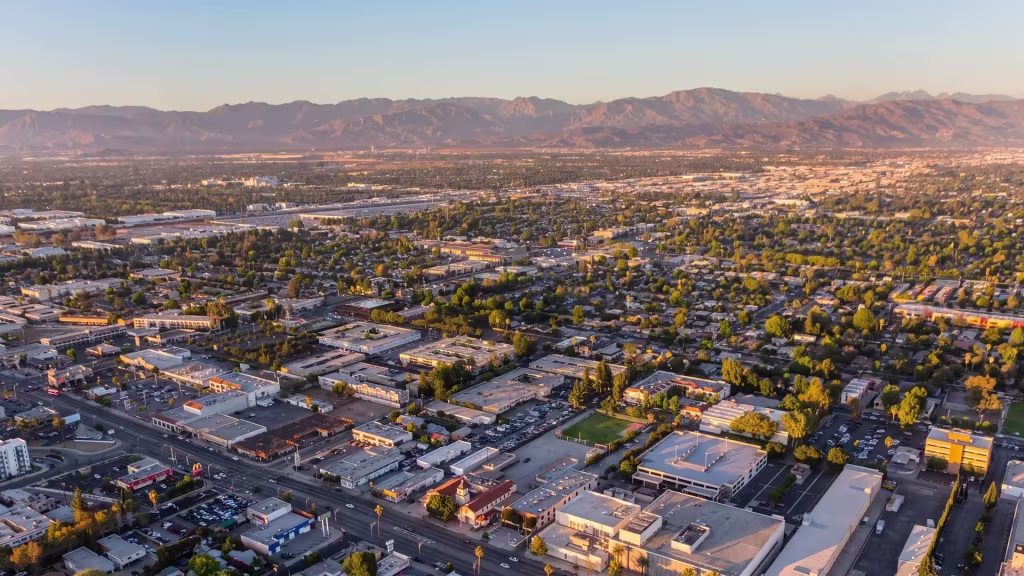 Aerial panorama over Van Nuys, a dense valley grid stretching toward mountains at sunset