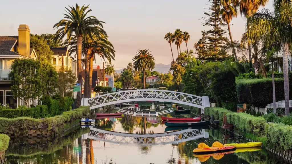 A landscaped canal in Venice curves past footbridges and waterfront homes, framed at ground level