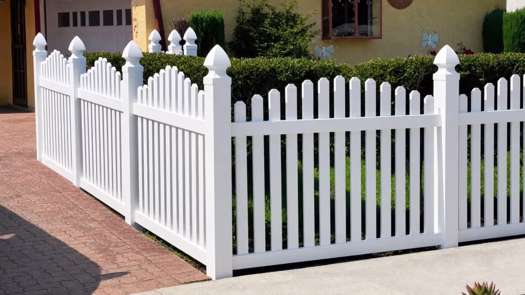 A stucco house wall decorated with butterfly ornaments backs this White vinyl arched picket fence run