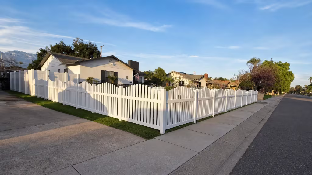 White vinyl arched picket fence rounding the corner of a front yard in a continuous wrap