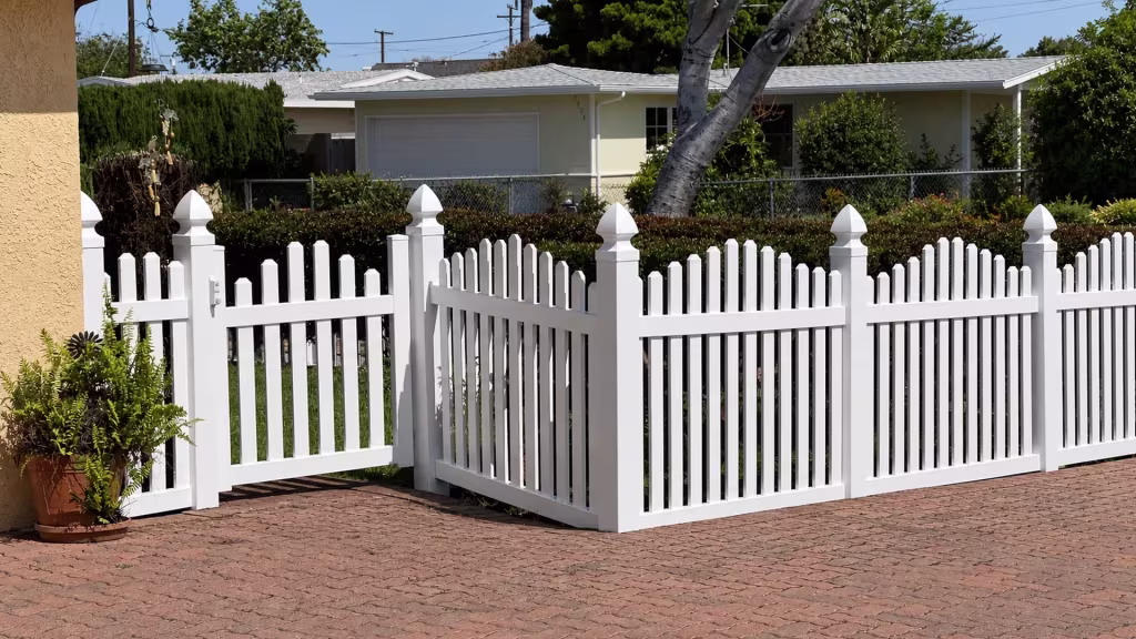 A single pedestrian gate with White latch hardware opens into this vinyl arched picket fence near a garage