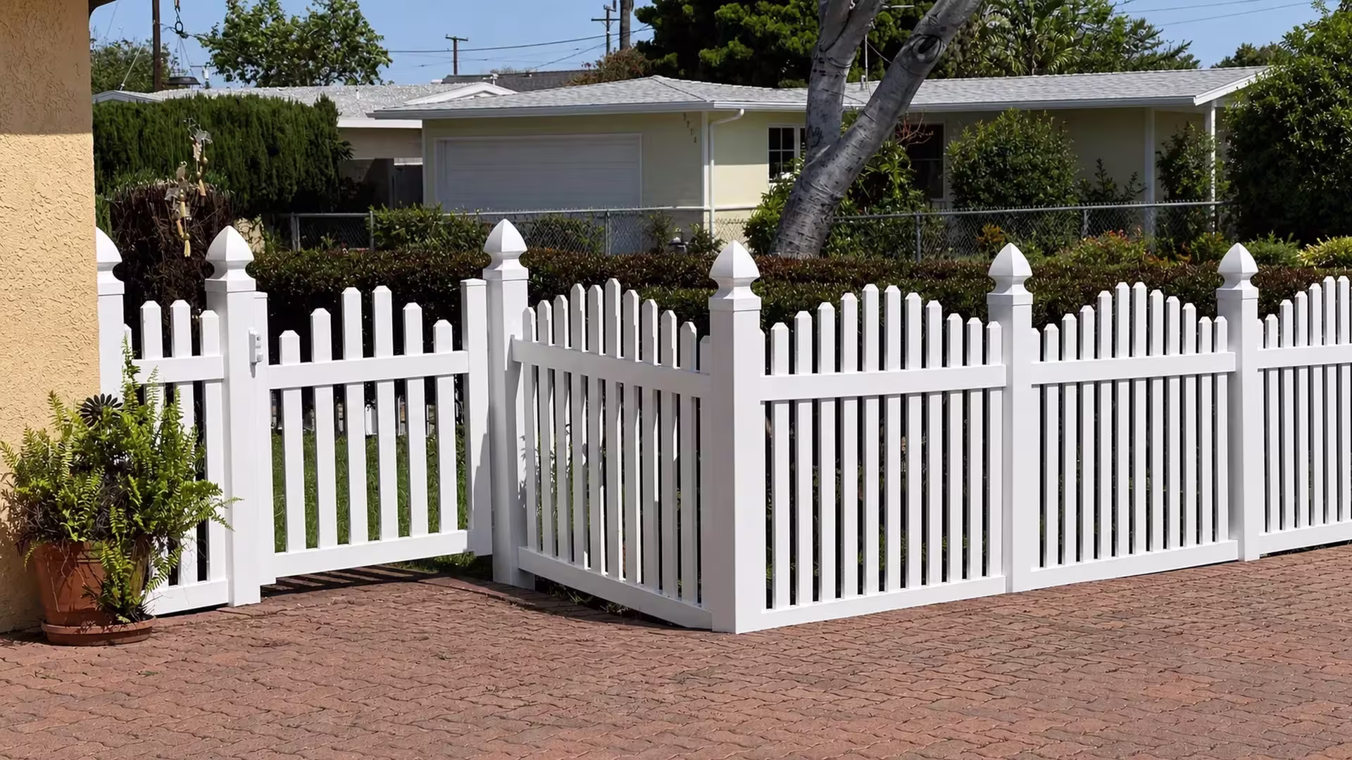 A single pedestrian gate with White latch hardware opens into this vinyl arched picket fence near a garage