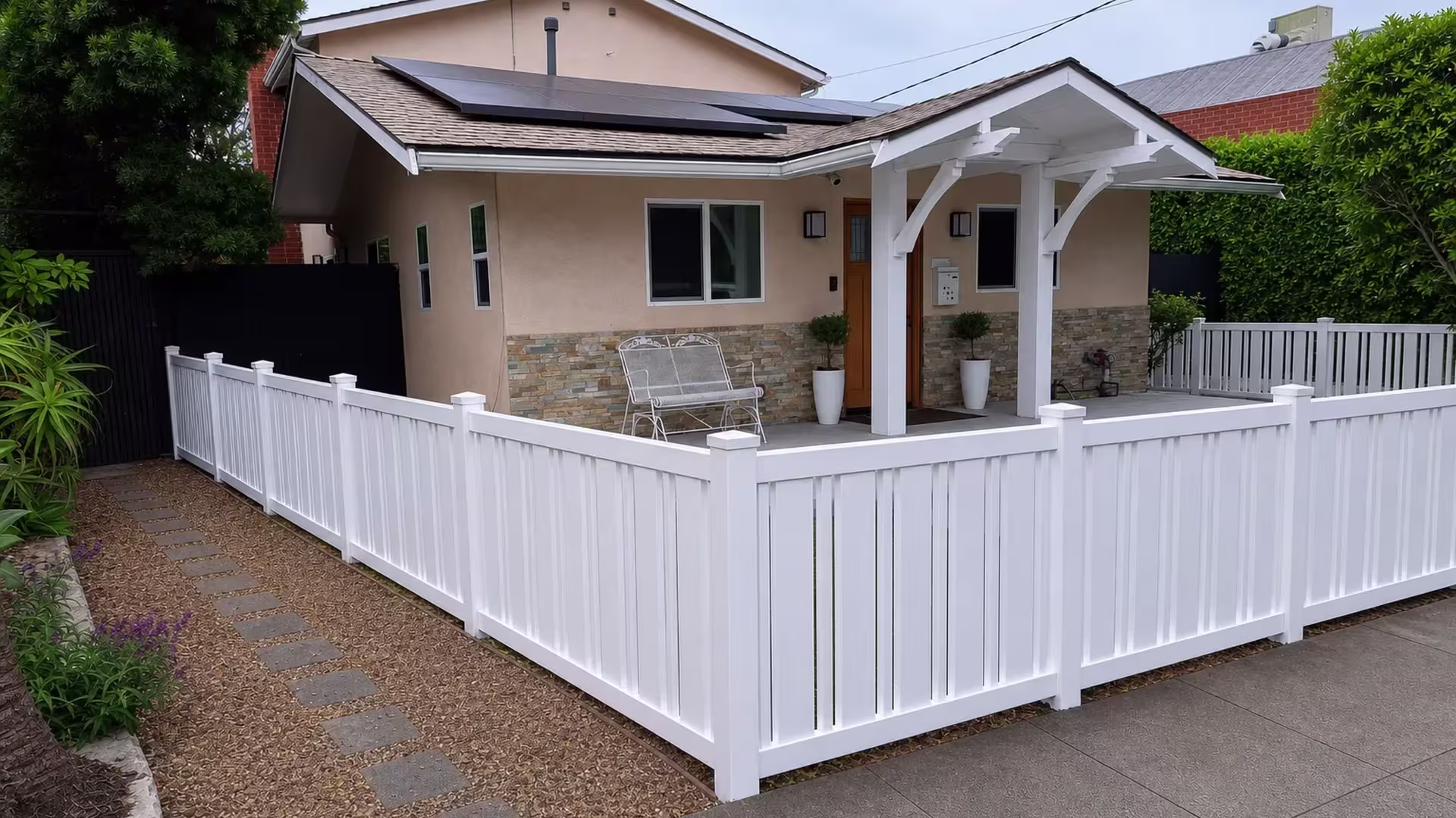 A picket run of Beige vinyl fence turns at a tall corner post near a stucco entry canopy