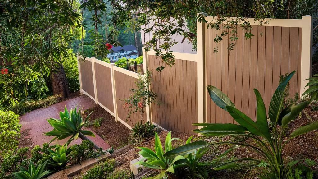 A stepped privacy line of Cream vinyl fence descends a steep planted garden slope in four sections