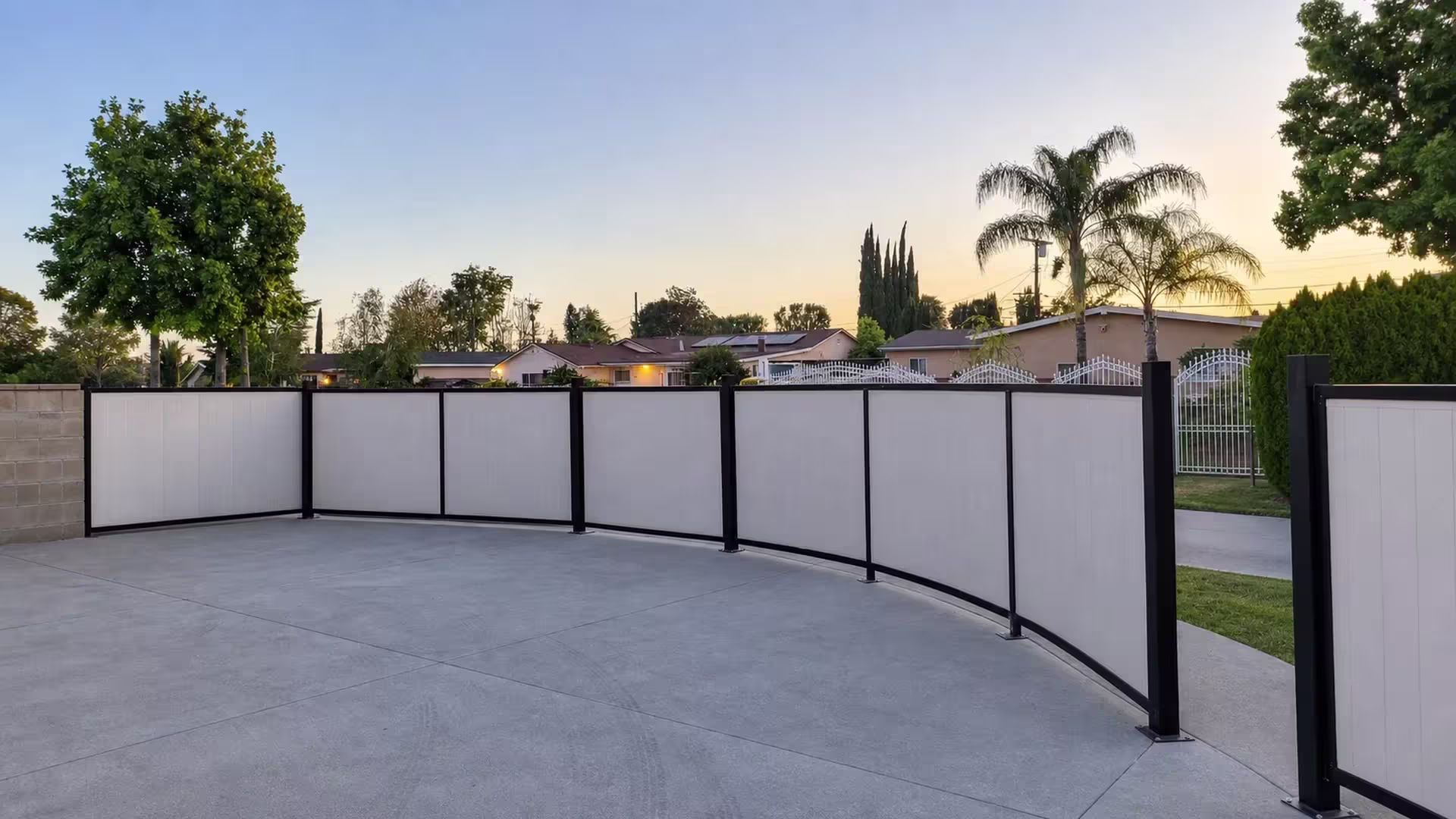 White vinyl custom fence in a black frame curving along a concrete driveway lined with palms and cypress trees