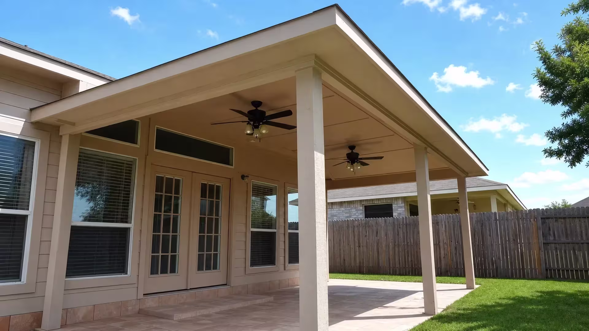 Tan vinyl custom patio cover attached along the rear wall of a house above a paved patio and lawn