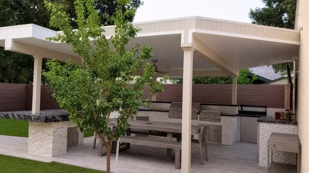 Tan vinyl custom patio cover shading a stone-faced outdoor kitchen and gray plank dining deck
