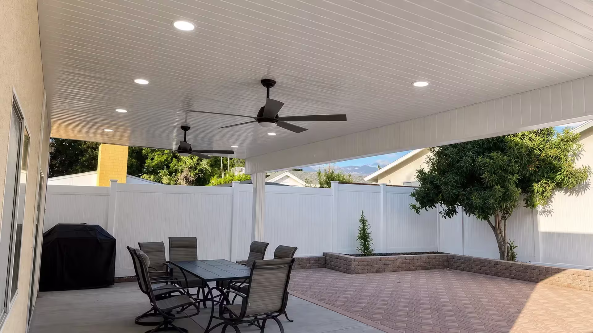Viewed from below, this White vinyl patio cover, custom built, shows ceiling fans and recessed lights along a stucco wall