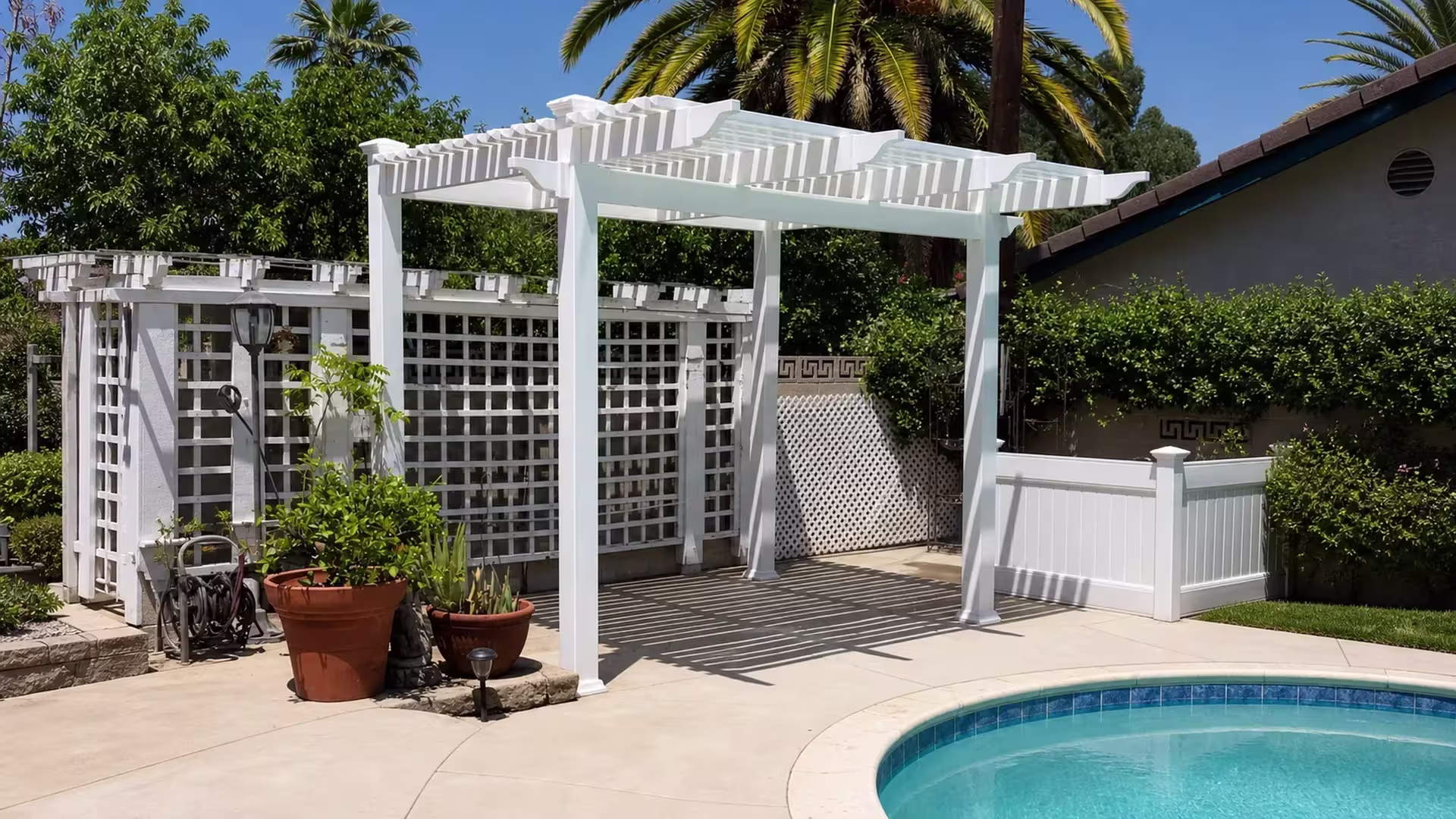 This freestanding open-lattice patio cover in custom White vinyl stands beside a curved pool with translucent roof strips