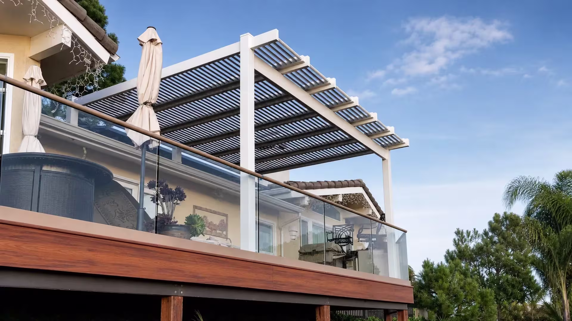 Dark gray cross rafters and louver blades top this louvered patio cover, custom made in White vinyl, above a raised deck