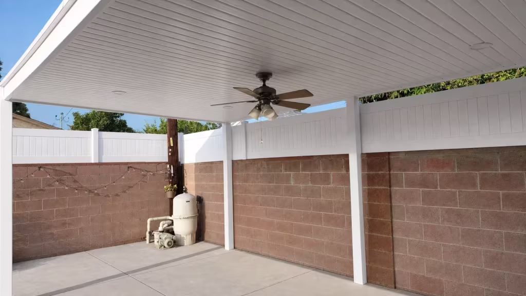 A solid ribbed roof caps this custom White vinyl patio cover above a concrete slab strung with lights near a masonry wall