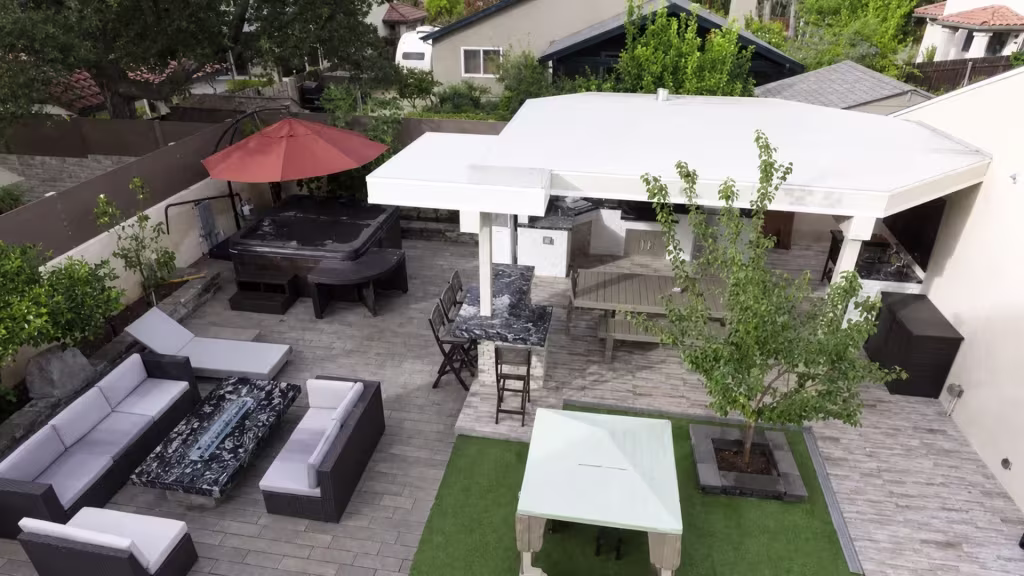 This custom-built patio cover in White vinyl offsets into a lower section, attached to a stucco house among mature trees