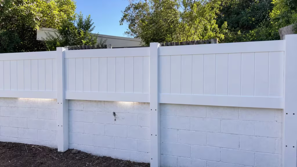 A White custom vinyl wall topper mounted level along a painted concrete block retaining wall