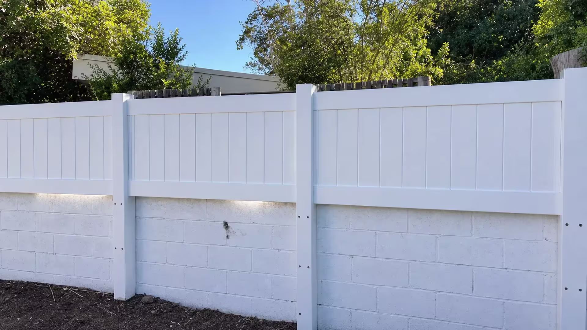 A White custom vinyl wall topper mounted level along a painted concrete block retaining wall