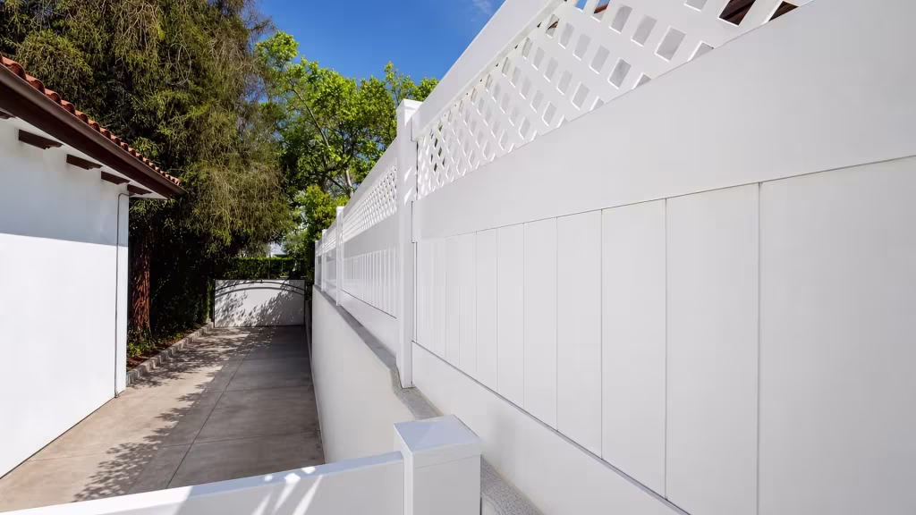 White custom vinyl wall topper following a stucco wall along a narrow driveway near a red tile roofline