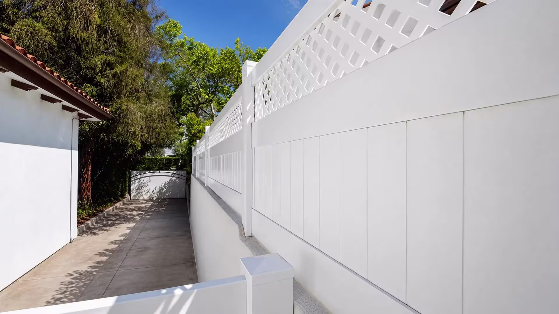 White custom vinyl wall topper following a stucco wall along a narrow driveway near a red tile roofline